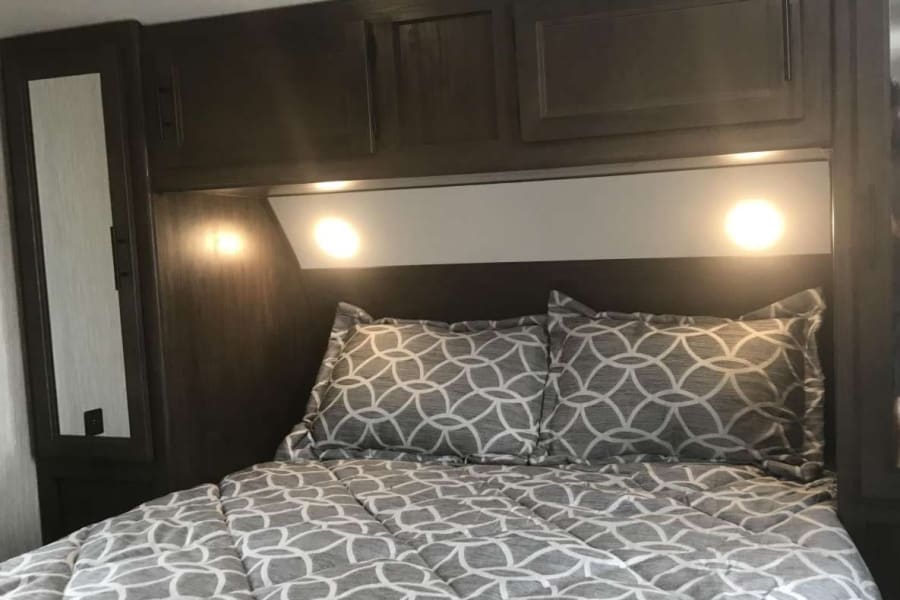 Cozy RV rental bedroom featuring patterned bedding, dark wood cabinetry, and bright reading lights. Perfect for your next adventure.
