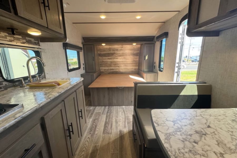 RV rental interior: kitchen with marble counters, convertible bed/dinette area, and a dining space with booth seating.