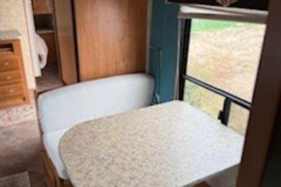 RV rental interior: A functional dinette with a speckled table and white benches, perfect for meals in your camper.