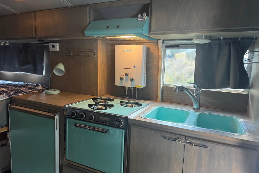 Cozy rv rental kitchen featuring a retro teal stove, sink, fridge, and wall-mounted water heater.
