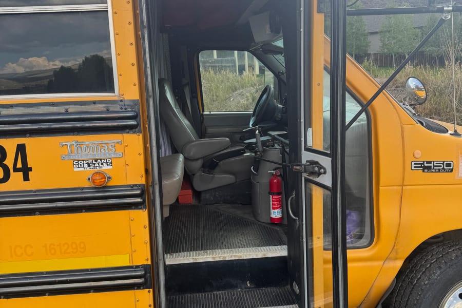 An open yellow school bus, possibly an RV rental conversion, reveals its driver's seat and interior steps, ready for adventure.