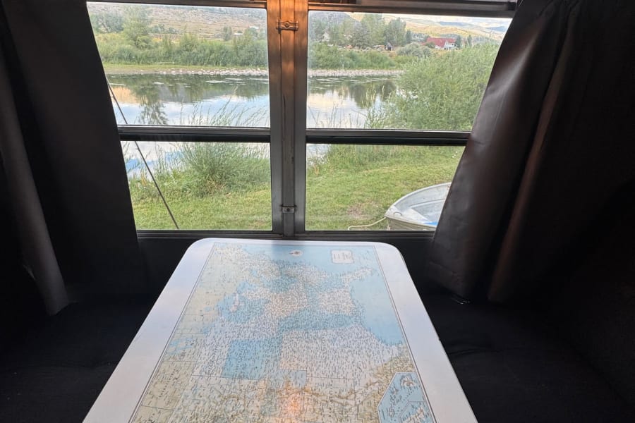 Cozy RV rental interior: map table, state plates, & a scenic river view from the window. Ideal for road trip adventures!