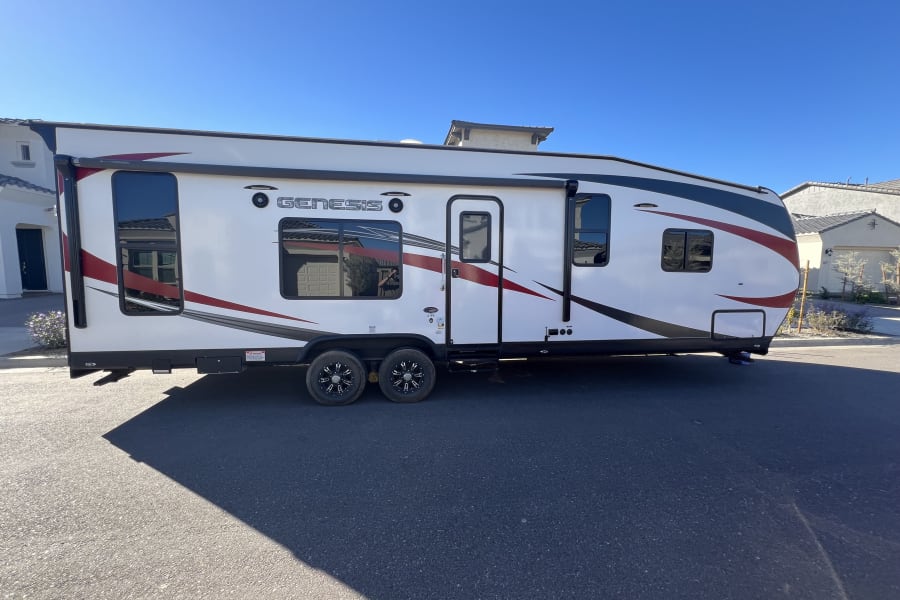 A white Genesis RV rental with red/black graphics is parked on a sunny street, ready for your next road trip adventure.
