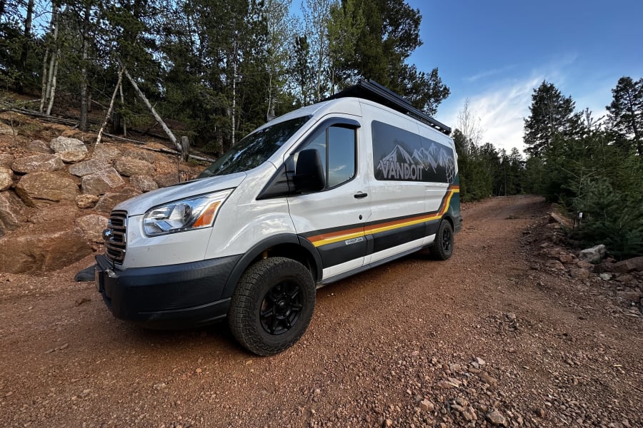 Adventure awaits with this RV rental! A white VANDOIT camper van on a rocky dirt road in a forest, ready for exploration.