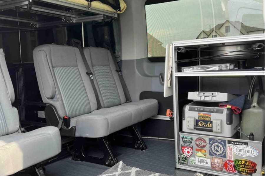 RV rental: well-equipped van interior with seating, overhead bunk, and fridge. Perfect for travel & camping adventures.