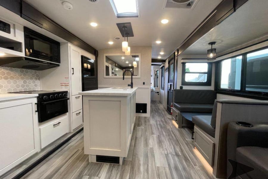 Modern RV rental interior showing a well-equipped kitchen with an island, and a comfortable living space with dinette seating.