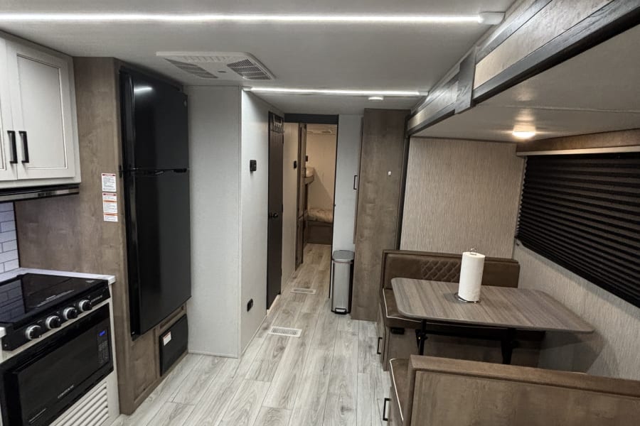 Modern RV rental interior: kitchen, dinette, and hallway with light wood flooring.