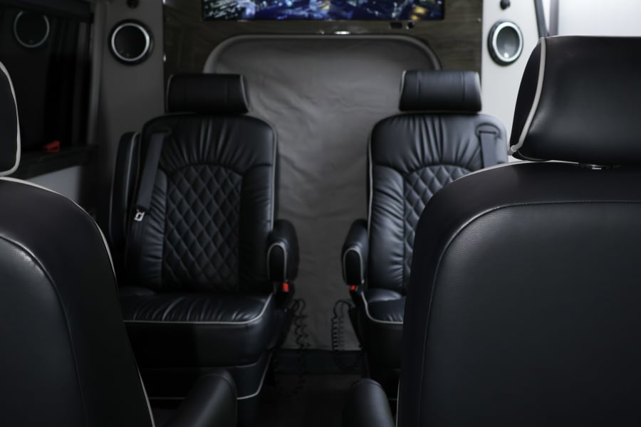 Luxury RV rental interior: black leather captain's chairs, a large TV displaying a cityscape, and mood lighting for comfort.
