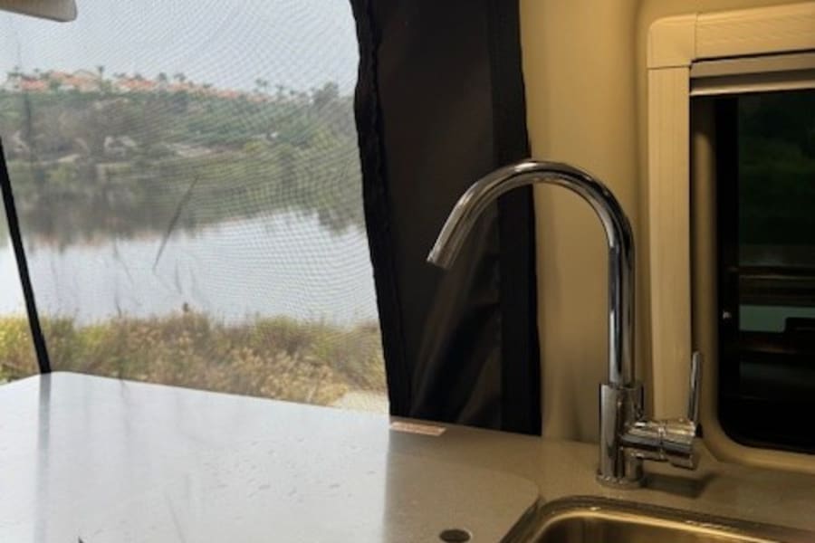 RV rental galley features a modern sink, spacious counter, and a stunning view of water and distant hills through the window.