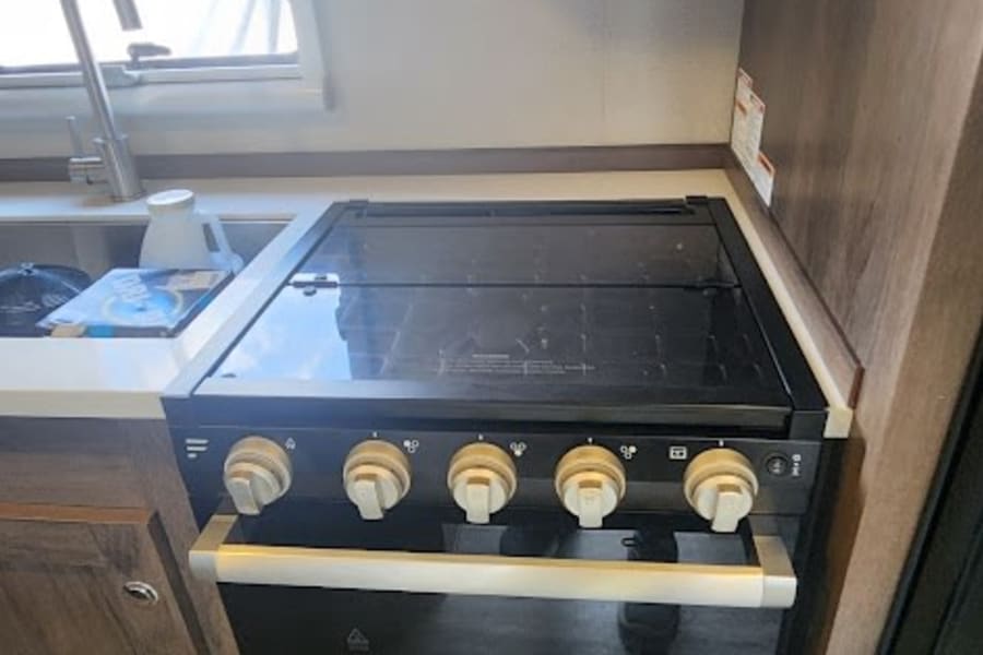 Compact RV rental kitchen featuring a black stove, oven, sink, and overhead range hood for easy cooking.