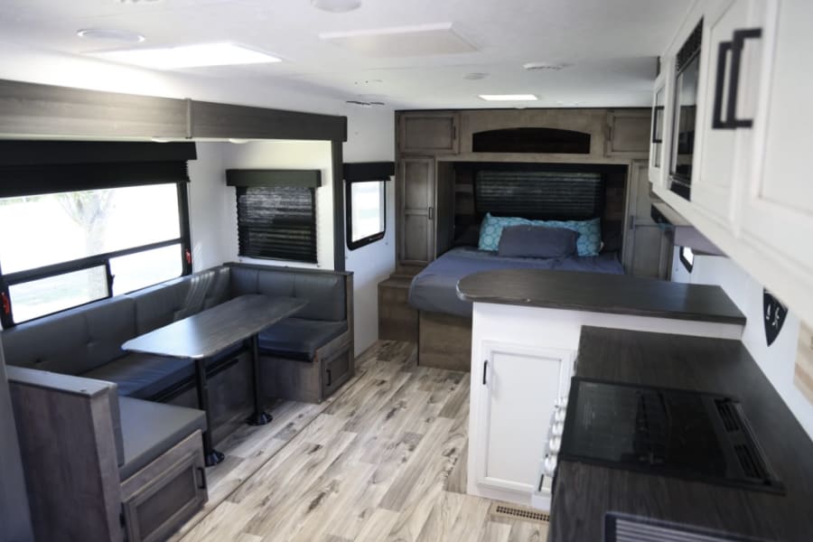 Modern RV rental interior showing a dinette, kitchen, and bedroom with contemporary finishes and light wood flooring.
