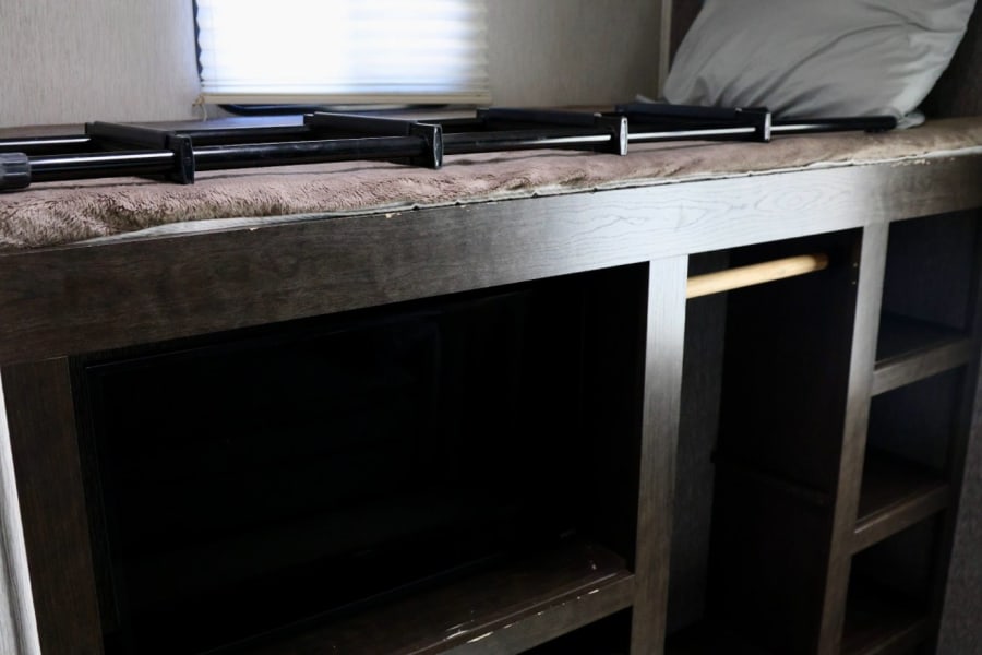 This RV rental features a bunk bed with safety rails above a TV and storage cabinets, providing a compact sleeping and media area.