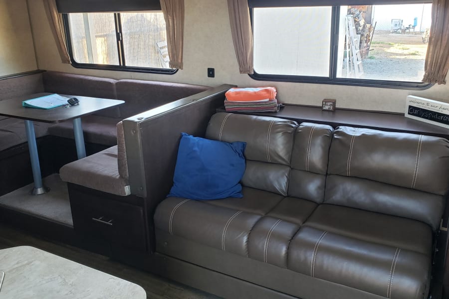 Cozy RV rental interior with a dinette, leather sofa, and welcoming signs, perfect for a comfortable travel experience.