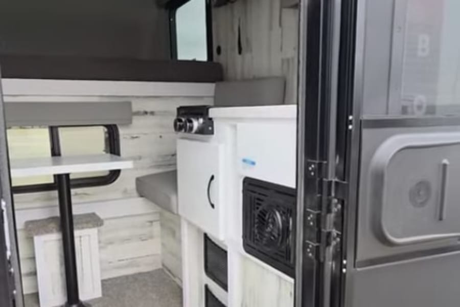 Cozy rv rental interior featuring a bunk bed, compact kitchenette, and dining booth with rustic wood-paneled walls.