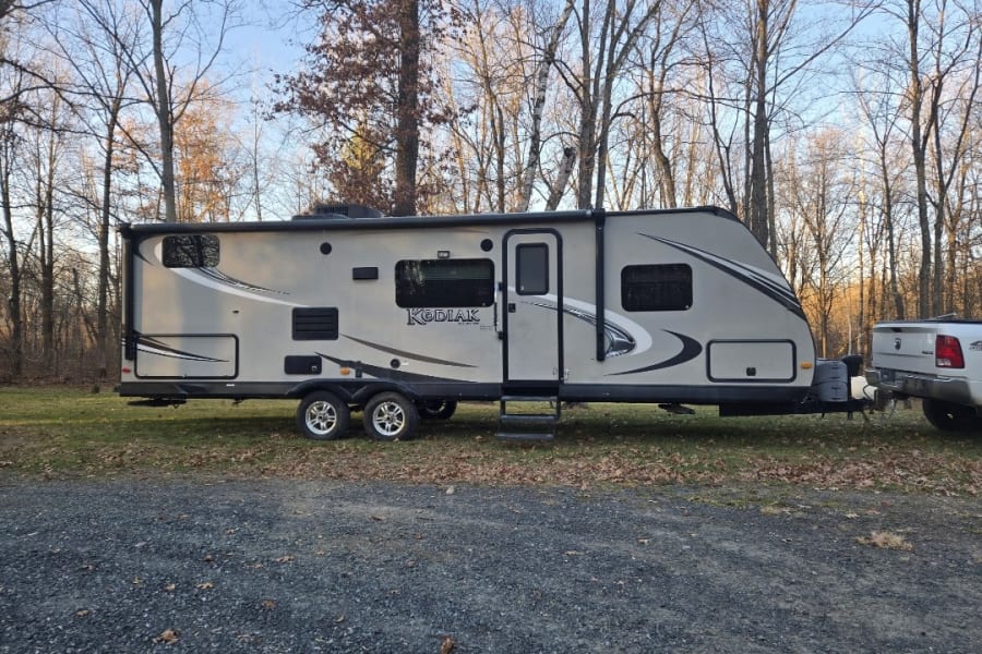 This Kodiak travel trailer RV rental, hooked to a pickup, is parked outdoors amidst bare trees, ready for your next adventure.