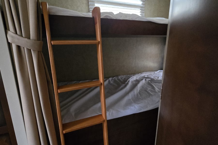 This RV rental features practical bunk beds with a wooden ladder, window, and privacy curtains, ideal for travel.
