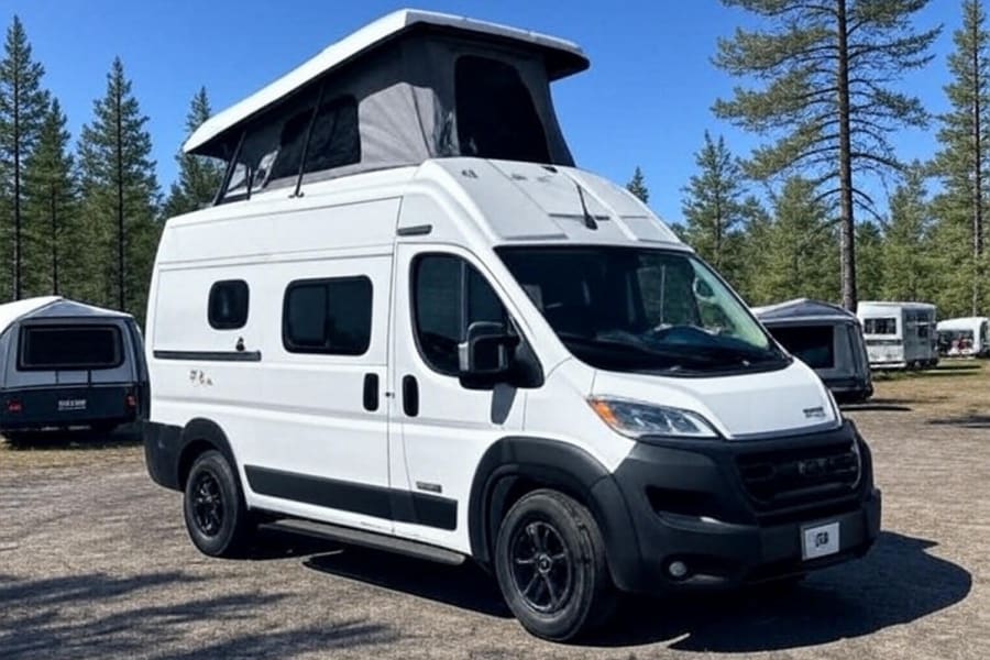 White pop-top camper van parked outdoors among trees, perfect for your next rv rental trip. Other RVs are in the background.