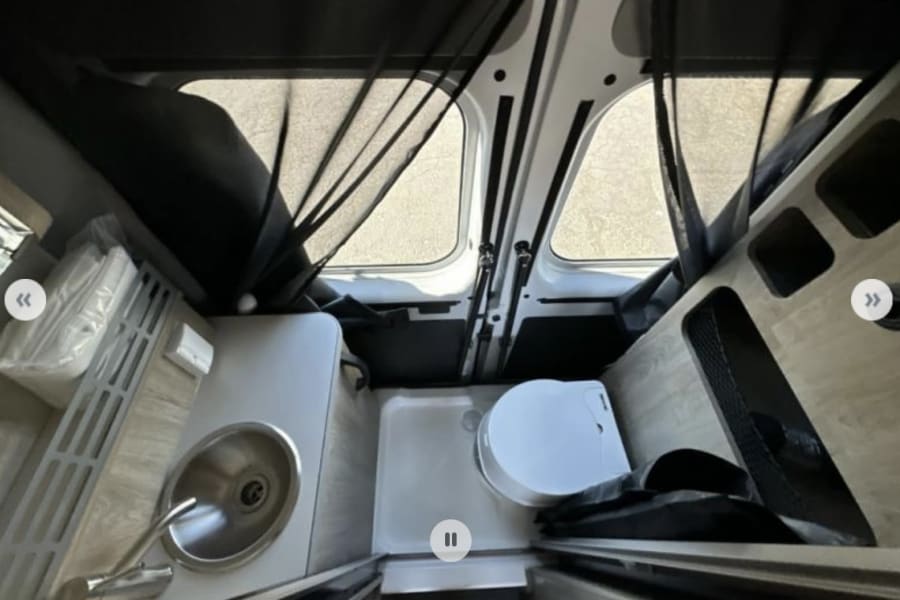 RV rental camper van interior: compact wet bath with toilet, shower pan, sink, and kitchenette area.