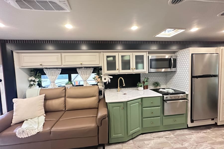 RV rental interior: a modern kitchen with green cabinets, white counters, stainless steel appliances, and a brown sofa.