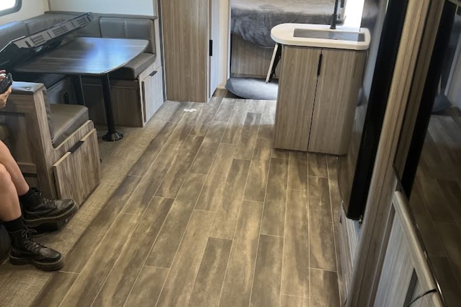 Bright RV rental interior showcasing wood-look flooring, a comfortable dinette, kitchen counter, and cozy bedroom in the back.