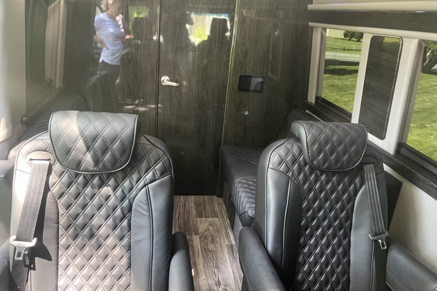 Inside a premium rv rental, showing black quilted leather seating, wood panels, and a clear reflection of a person on the left.