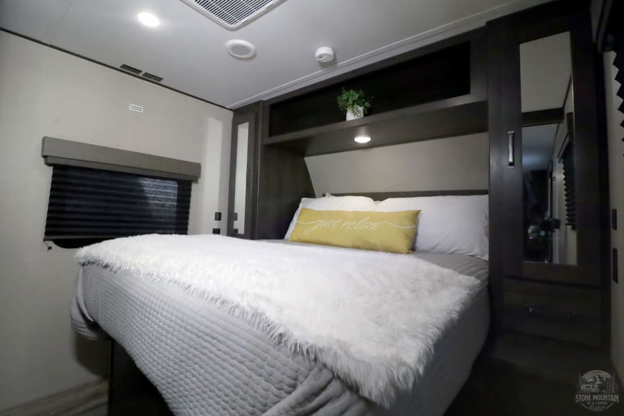 Cozy RV rental bedroom interior: comfortable bed, window, and overhead storage for a relaxing getaway.