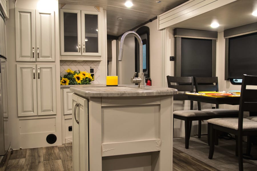 Explore this bright rv rental's kitchen and dining area, complete with an island sink, sleek cabinets, and a comfortable table.