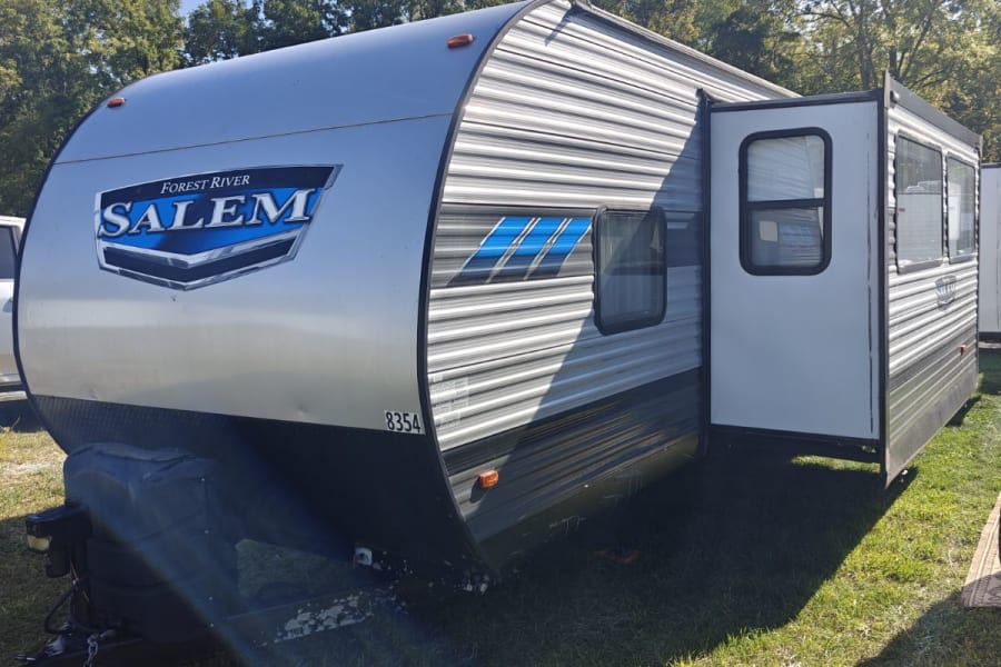 Forest River Salem travel trailer, perfect for rv rental. Silver & black, door open, on sunny grass, sunny day.