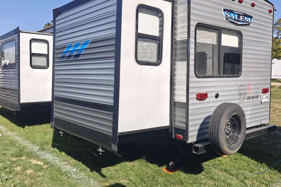 Two modern RVs with extended slide-outs, gray and white, parked on green grass under a blue sky, ready for rv rental.