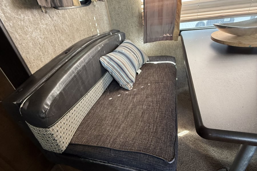 Cozy rv rental interior featuring a dark brown dinette bench with a striped pillow, a table, and windows with blinds.