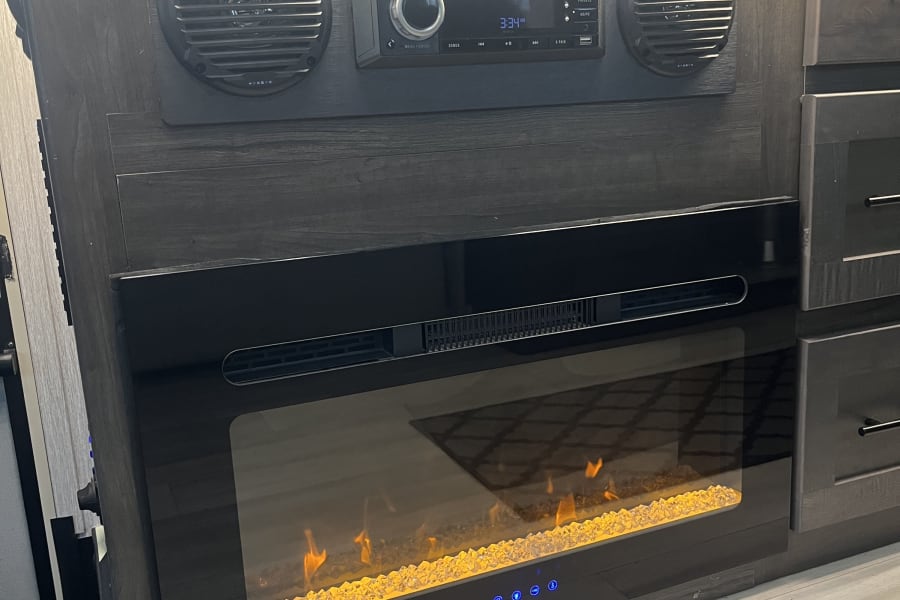 Modern RV rental interior featuring a cozy electric fireplace, stereo system, and LED lighting for comfortable travel.