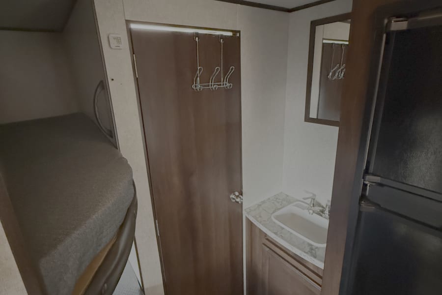Inside an rv rental: bunk beds, a compact vanity with sink, door with hooks, and built-in refrigerator.