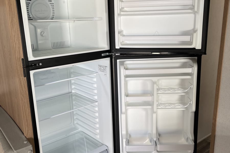 An empty two-door refrigerator and freezer unit inside an rv rental, highlighting its clean shelves and efficient interior layout.