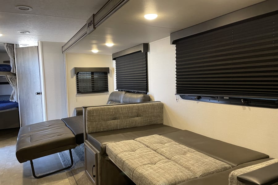 RV rental interior: A versatile lounge/dinette converts to a bed, featuring bunk beds, black blinds, and bright overhead lights.