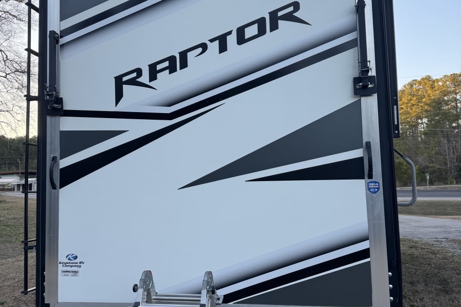 Rear view of a white & black "Raptor" toy hauler RV. A ladder leans on its ramp door. Great for rv rental camping trips.