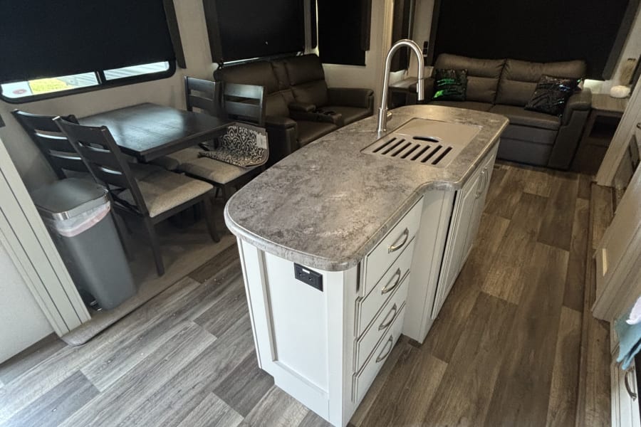 Spacious RV rental interior featuring kitchen island, dining table, and living area. Wood-look flooring, modern lights.
