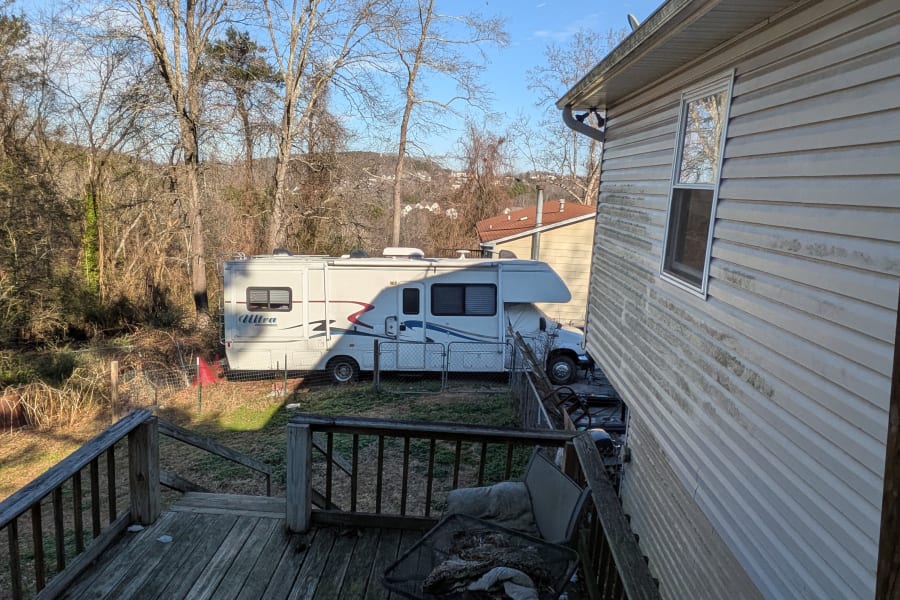 View of a white motorhome (Ultra RV) parked in a fenced yard, seen from a deck. Considering an rv rental for your next trip?