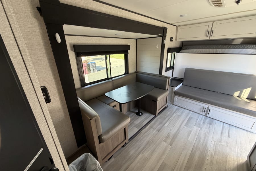 Modern rv rental interior with a U-shaped dinette, table, and a versatile sofa that converts to a bunk bed.