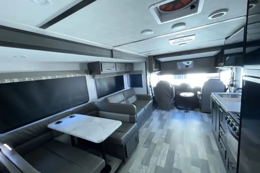 Spacious RV rental interior: modern living area, dinette, kitchen, and driver's cockpit.