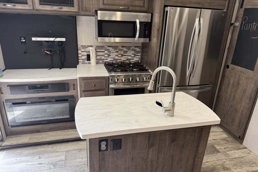 Well-equipped rv rental kitchen featuring an island sink, full stainless steel appliances, fireplace, and entertainment area.
