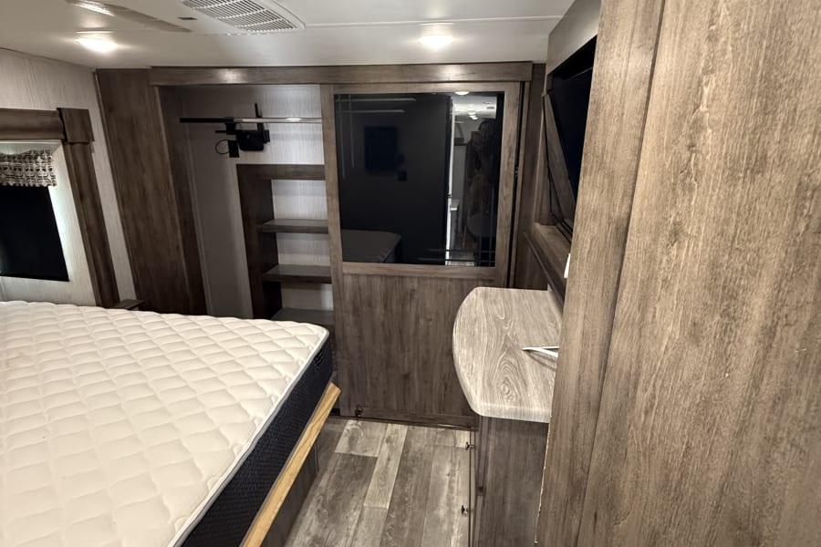 Cozy RV rental bedroom features a plush mattress, wood-look flooring, built-in storage, and modern cabinetry.