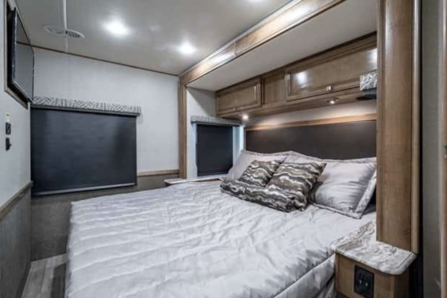 RV rental bedroom featuring a spacious bed, overhead cabinets, roller blinds, and a TV for ultimate comfort.