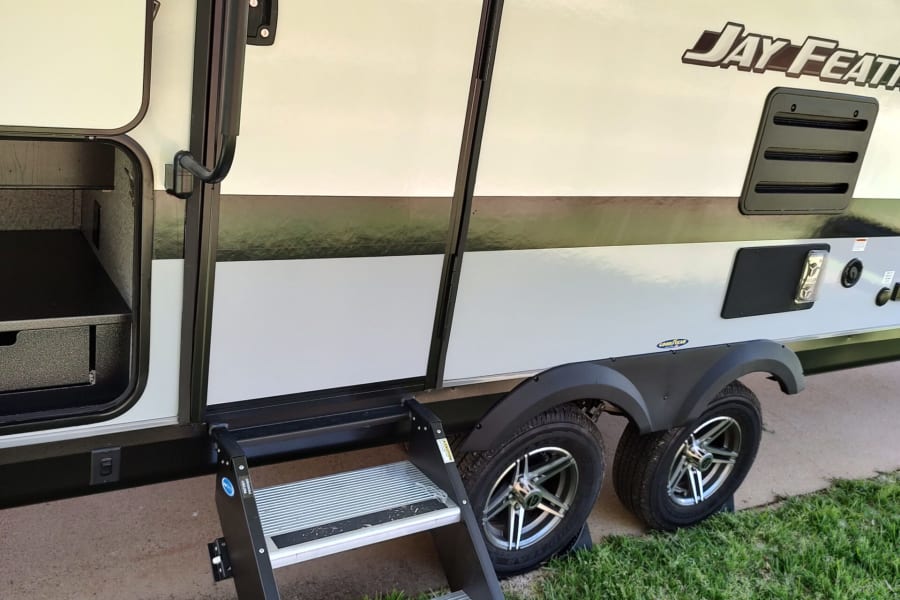 This RV rental features an open storage, entry door with handle, and extended steps. Dual wheels are visible on the side.
