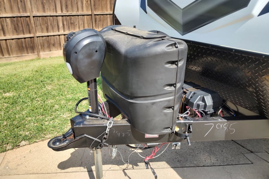 Close-up of an RV rental's front hitch with propane tank cover, power jack, battery box, and safety chains. Essential travel gear.