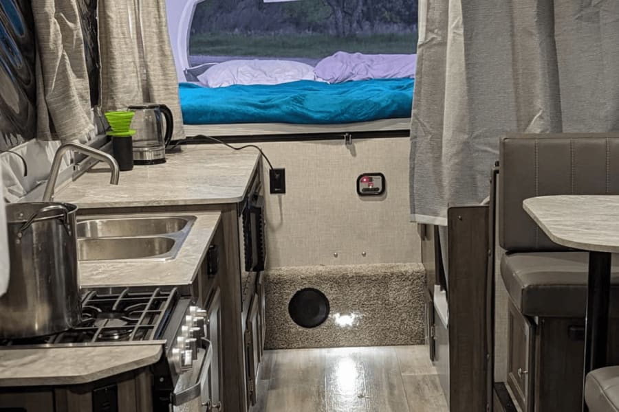 Compact RV rental interior: a functional kitchen (sink, stove), a cozy dinette, and a comfy bed are ready for your next trip.
