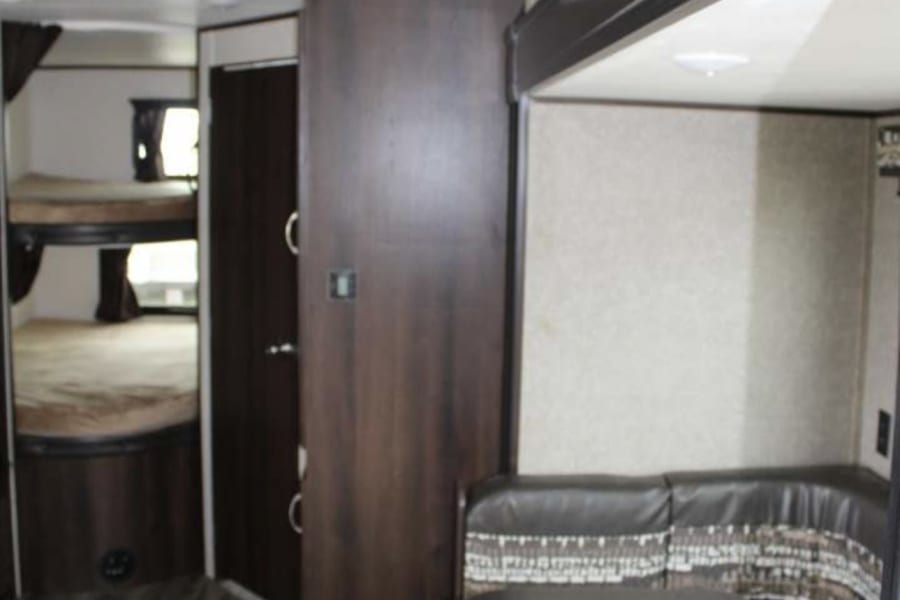 Interior of an RV rental featuring bunk beds on the left and a U-shaped dinette with a table on the right.