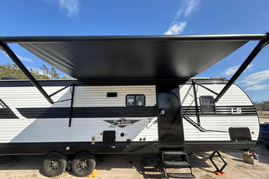 Extended awning shades this Shasta travel trailer, perfect for your next RV rental adventure under a clear sky.