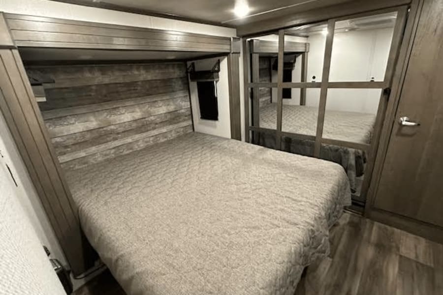 Experience comfort in this RV rental bedroom, featuring a cozy bed, wood-paneled accent wall, and mirrored closet.