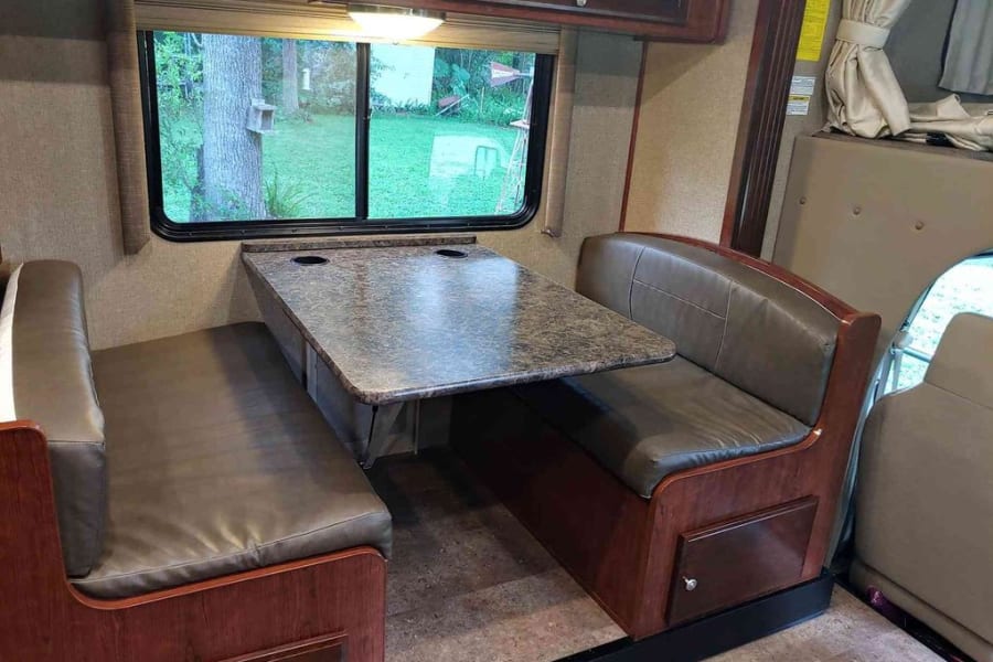 This RV rental features a cozy dinette with booth seating, a table with cupholders, and a scenic window view.