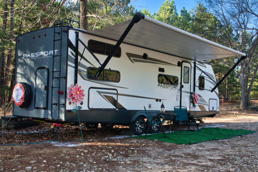 White Passport travel trailer rv rental parked at a scenic campsite, featuring an extended awning and outdoor seating.